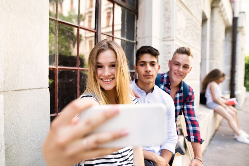 College freshman girl snaps a selfie of her and her friends on the university grounds, in a representation by models.