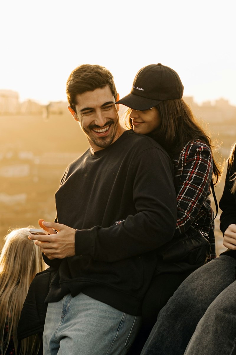 A photo depicting a man and a woman embracing while sitting on top of a hill.