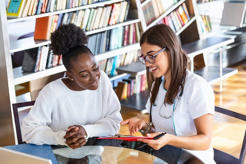 Academic advisor and a student work together in a library setting, as represented by 2 models.