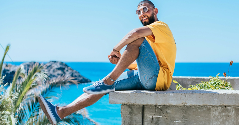 A model representing a man on vacation, sitting on the edge of a concrete wall by the ocean
