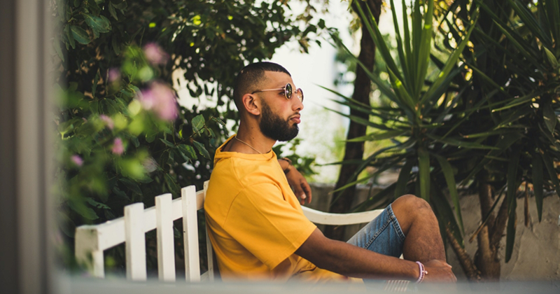 A model representing a man on vacation, sitting on a bench surrounded by greenery