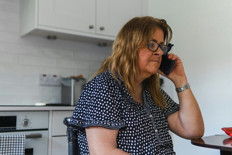 Woman sitting in the kitchen talking over the phone.