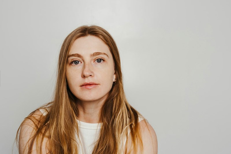 Woman in a white sleeveless top looking serious against a plain light background.