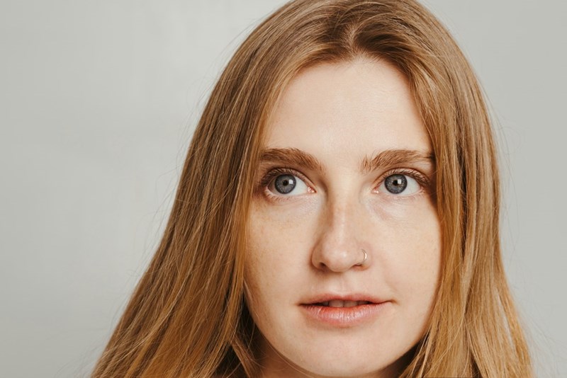 Close-up portrait of a serious woman with red hair against a plain light background.