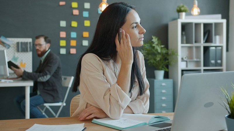 An office employee sits at her desk looking away from her laptop while working in a modern workplace.