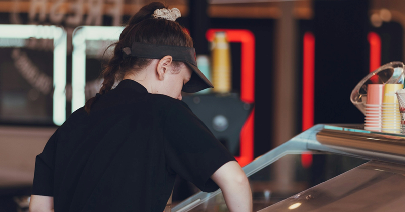 A representation of a young female fast food worker cleaning a metal counter