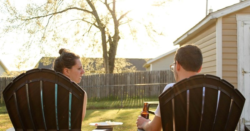 Two models (not actual subjects) sit in lawn chais in the backyard of a house.