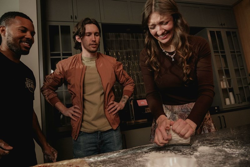 Two men and a woman cooking bread in the kitchen.