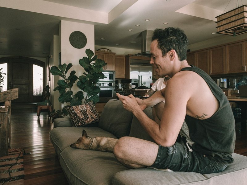 Man laying in a brown couch using his cellphone.