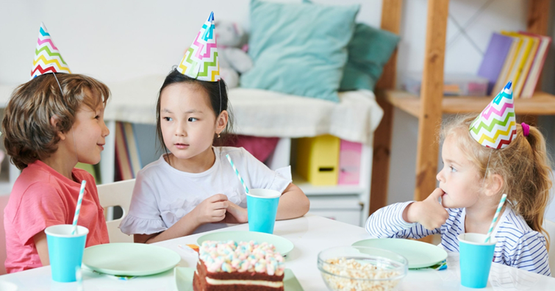 A representation of three young girls sitting at a table wearing party hats, having a discussion