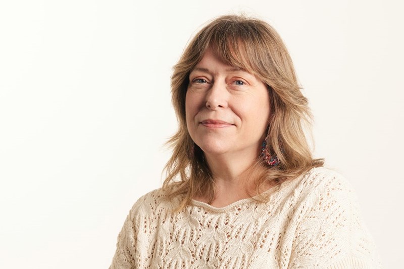 A confident middle-aged woman poses for a portrait against a clean background.