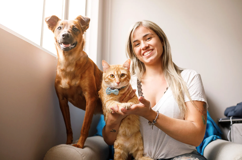 Woman sitting with dog and cat near a window.