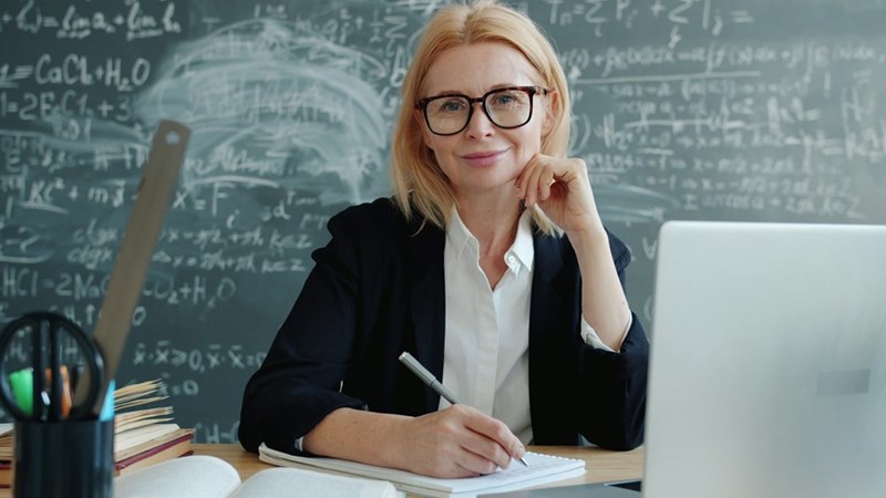 Confident academic taking notes at her desk with a background of mathematical formulas and diagrams.