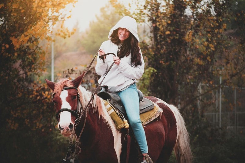 Happy teen practices riding a horse during her lesson, in a depiction by a model.