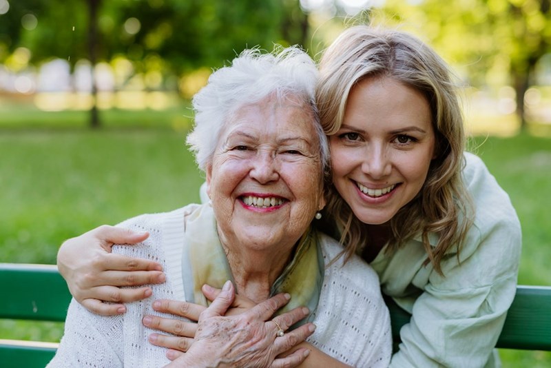 A smiling grandmother and granddaughter share a joyful moment together in a sunny park.