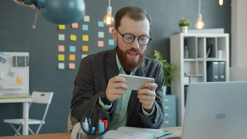 A professional checks his phone while taking a quick break at his desk in a modern office.