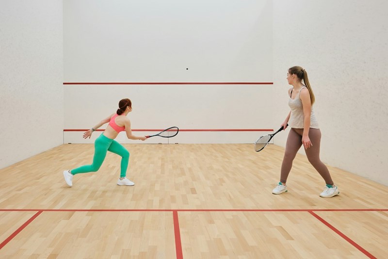 A representation of two women playing squash at an indoor court.
