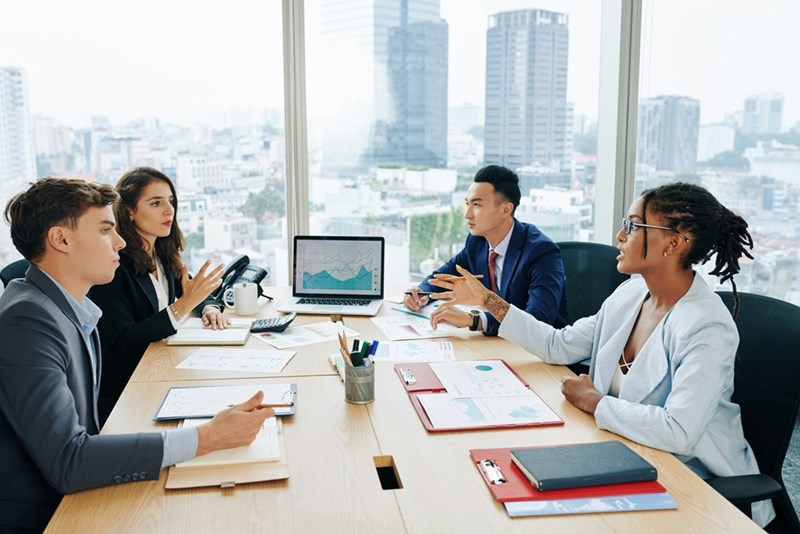 A fictional representation of employees gathered around a table during an office presentation.