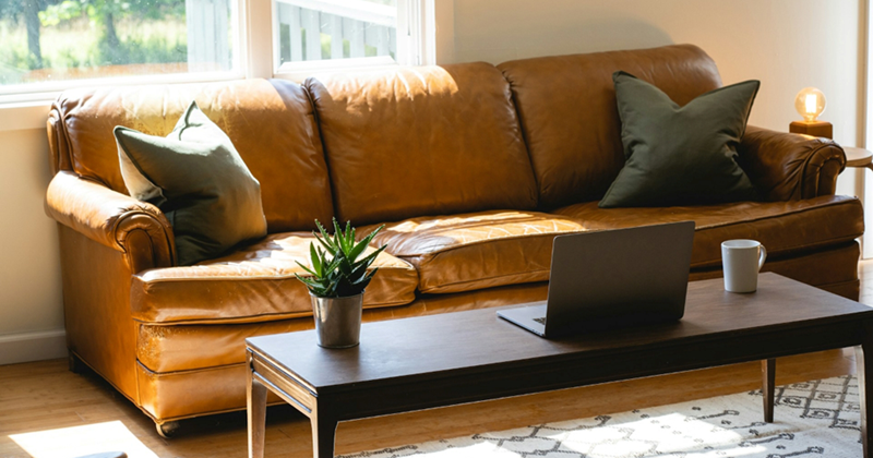 A representation of a couch in a living room with a laptop placed on the coffee table in front of it