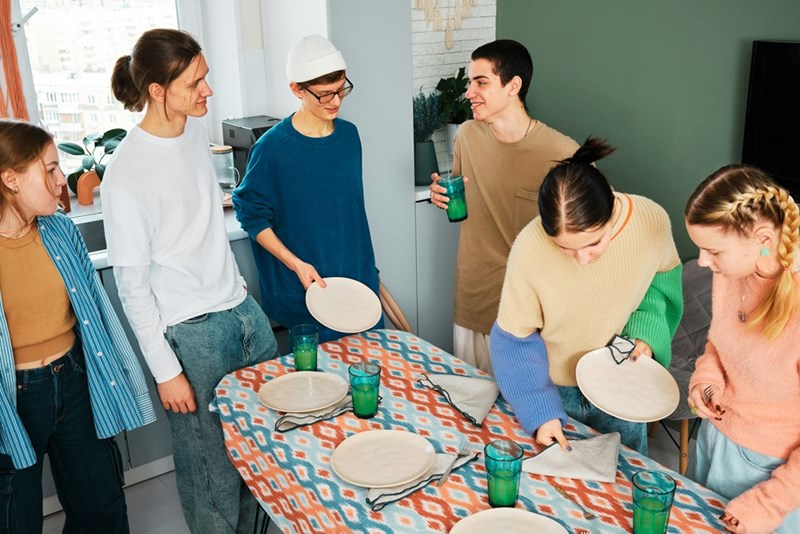 A photograph of a group of friends standing around a table with empty plates at a dinner party. Not the actual subjects.