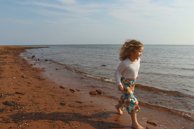 Little girl plays on the beach, in a depiction by a model.