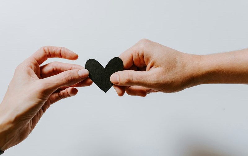 two people holding a black papercut heart