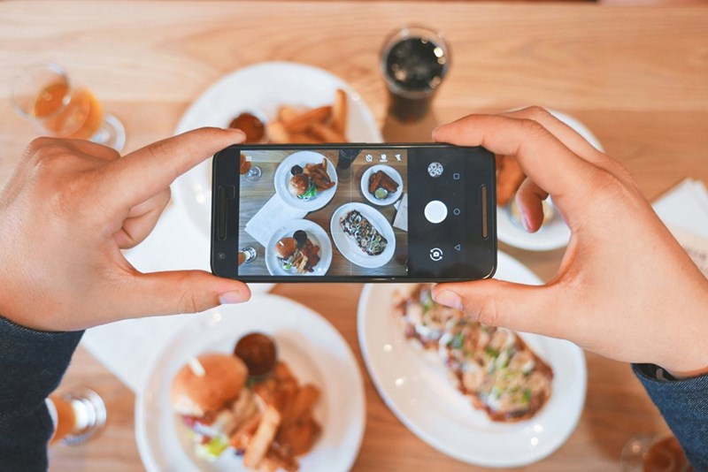 Influencer snaps a photo of an aesthetically pleasing restaurant meal, as represented by a model.