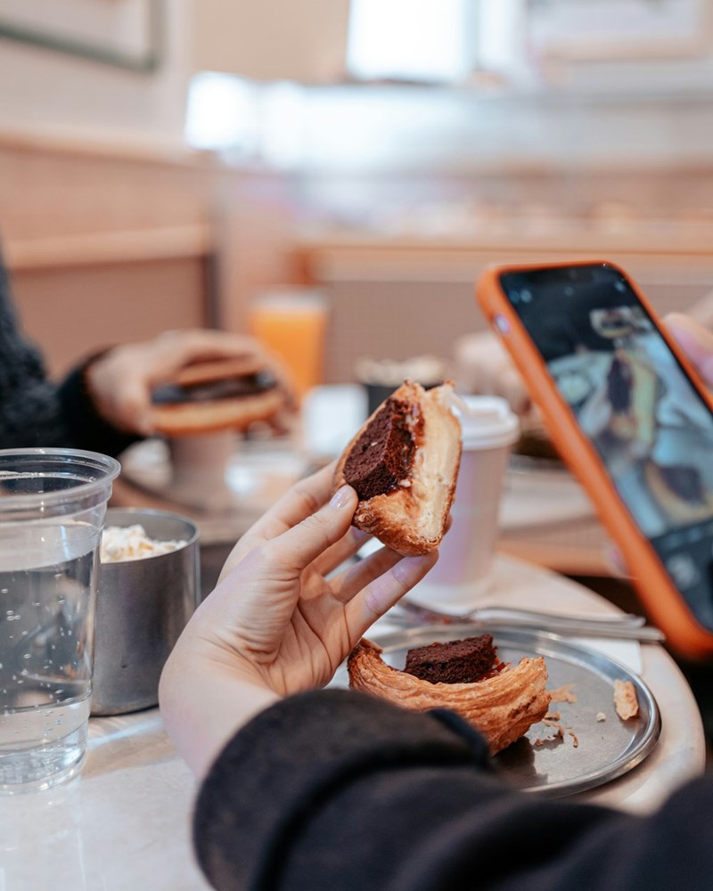 Food influencer holds hand at an awkward angle to get the right photo of a pastry, in a representation by a model.