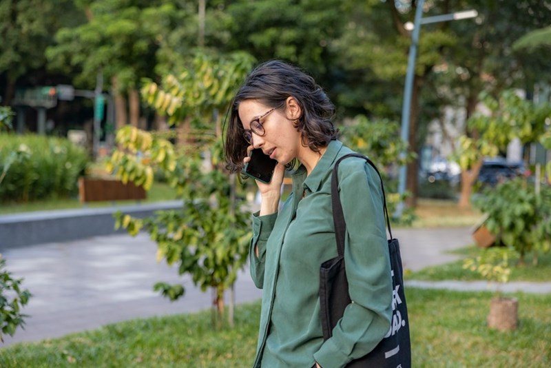 A concerned woman wearing glasses talking on a cellphone in a park.