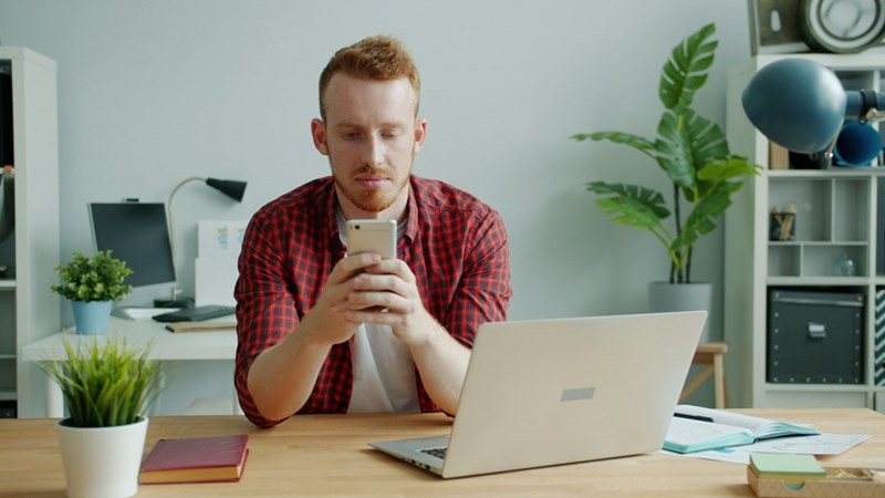 Office employee checking smartphone messages during a productive workday at his desk.