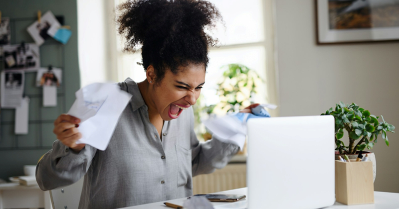 A model representing a frustrated employee yelling and scrunching paper in her hands while sitting behind a laptop