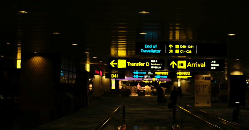 A representation of a dark airport hallway at night with neon directional signs