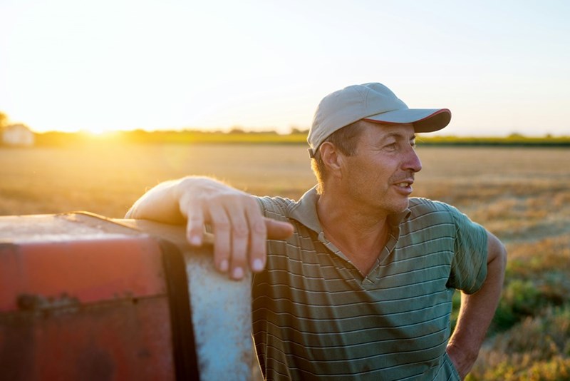 A farmer leans against his machinery in the middle of his field to discuss something (stock).