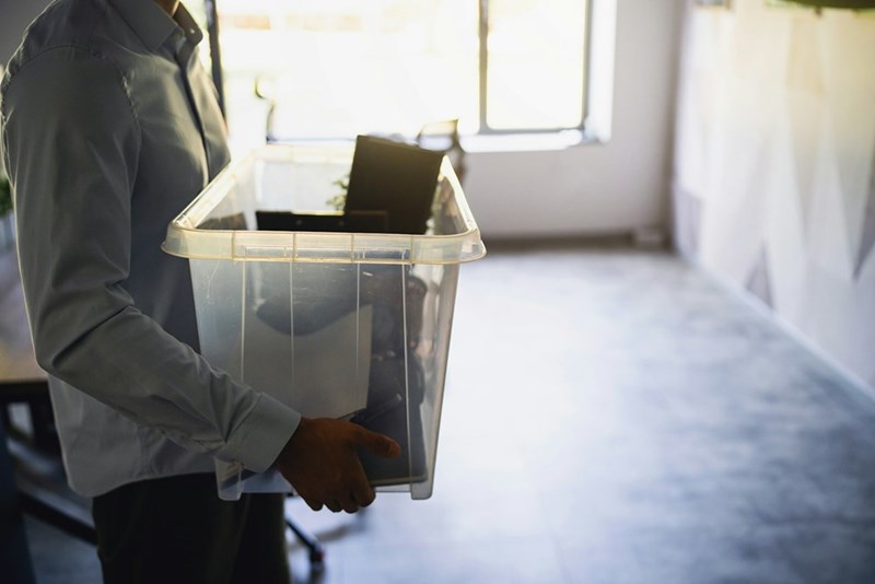 Person carrying a plastic storage bin containing office equipment and personal belongings