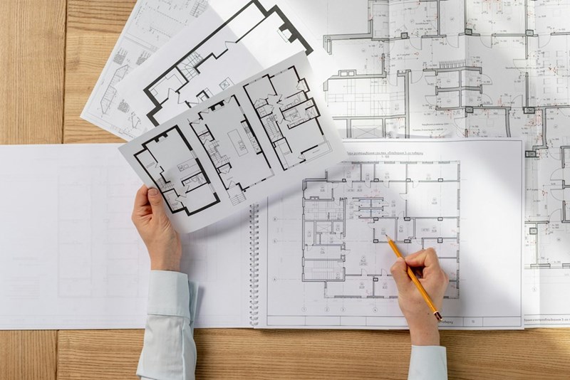 Hands reviewing architectural floor plans and technical building drawings on a table.