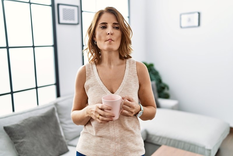 Woman holding a mug in a bright living room, looking unimpressed and firm.