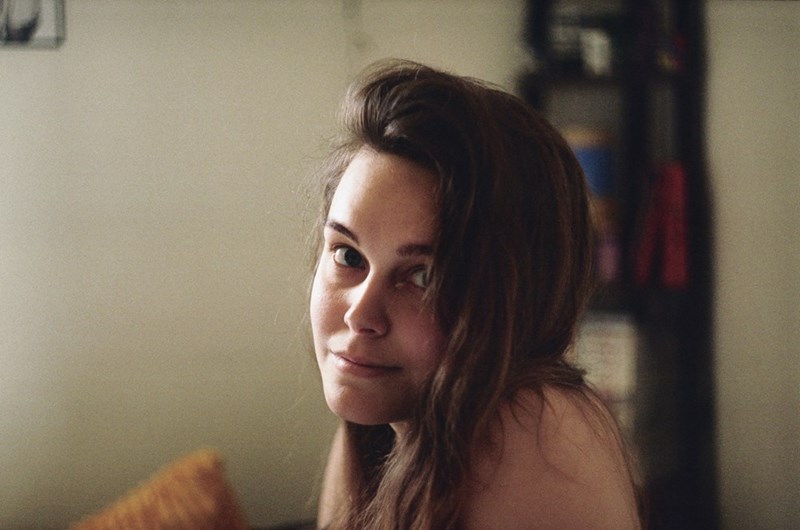Woman sitting indoors looking into the camera lens with a slightly amused and slightly confused expression