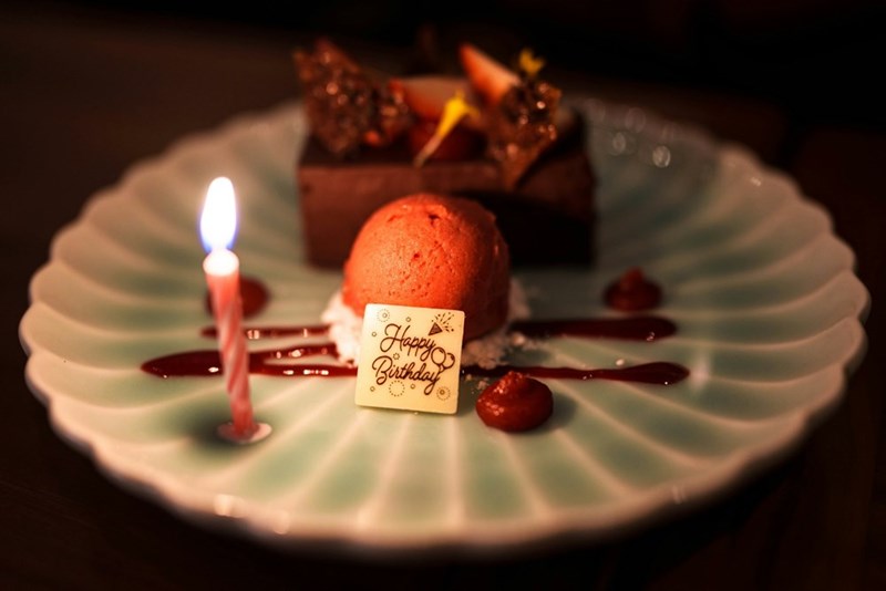 A birthday dessert is served with a lit candle on an elegant plate.