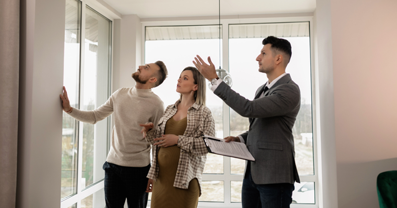 A couple viewing a house for sale with a real estate agent, represented by models.