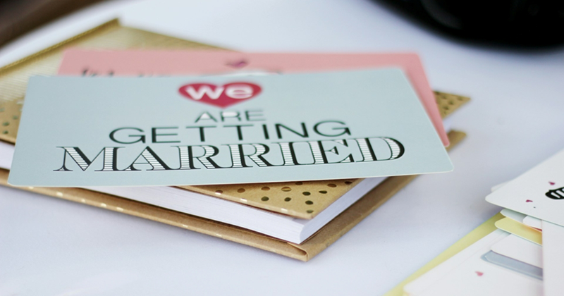 A representation of a wedding invitation that says ‘we are getting married’ sitting on top of a notebook