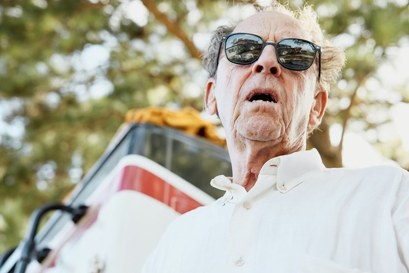A grumpy old man wears sunglasses and yells at someone in the distance (model).