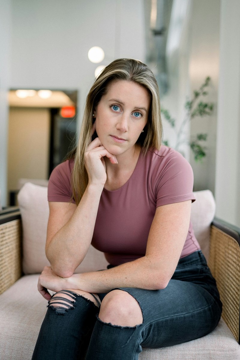 Woman sitting indoors in an armchair, looking serious and thoughtful with her hand under her chin.