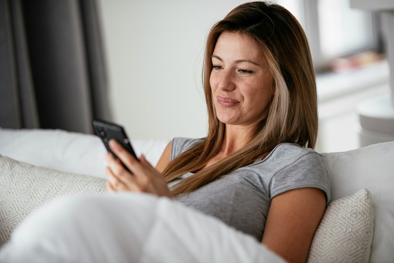 Woman lying in bed and smiling while reading something on her phone.