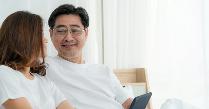 A man holding a tablet looks at a woman as they sit in bed together