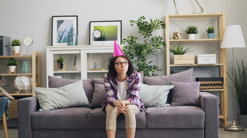 a woman wearing a birthday hat sitting on a couch alone
