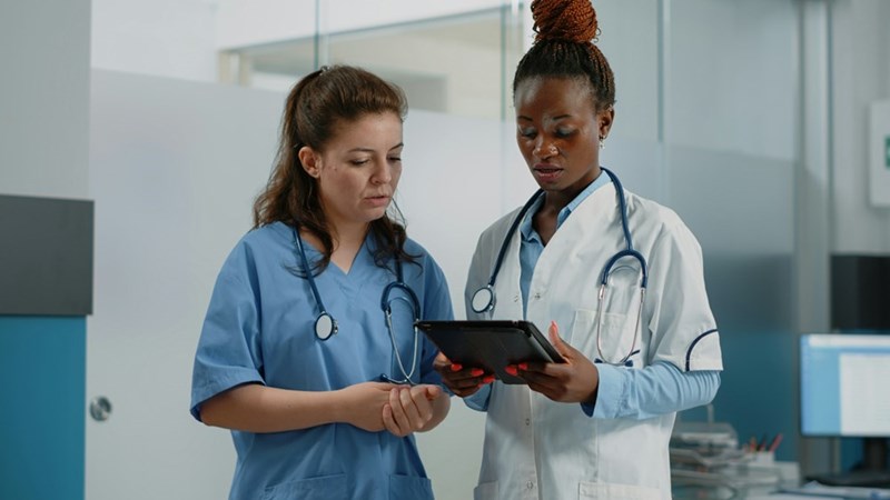 A representation of two healthcare workers discussing information on a tablet in a hospital.