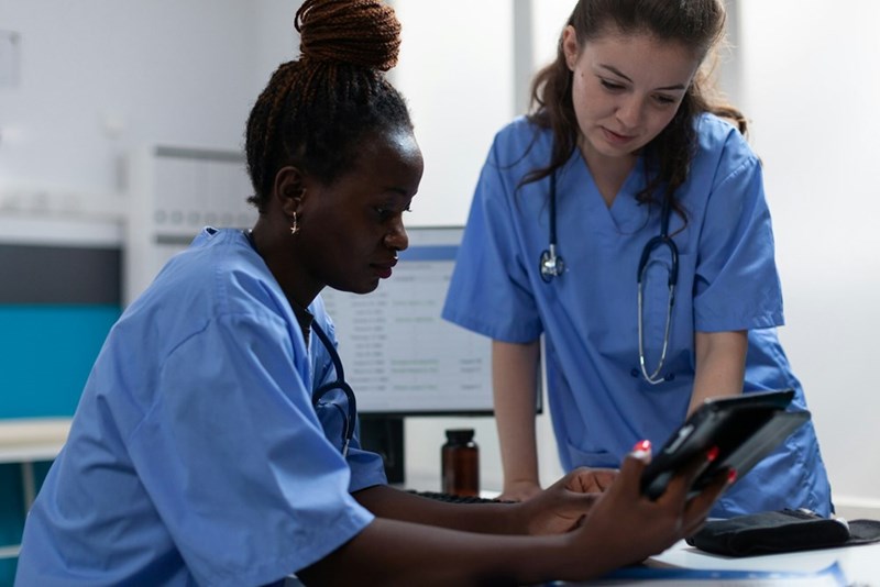 A representation of two hospital employees reviewing data together on a tablet.