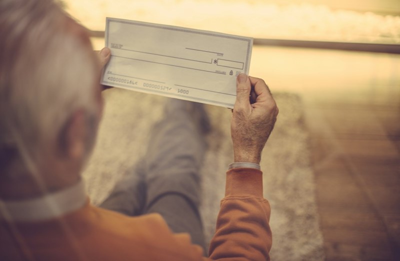 An elderly man, the landlord, looking at a bank check, represented by a model.