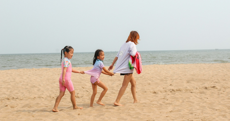 A representation of a mom and two daughters walking across a beach during the day