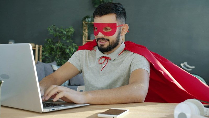 Man in a superhero costume working on a laptop, depicted by a model.